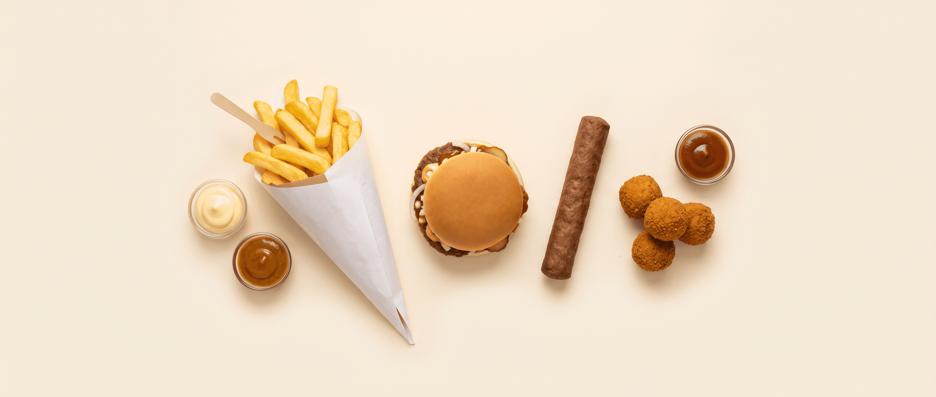 Belgische frituursnacks van bovenaf: een puntzak frieten, een bicky burger, een frikandel, bitterballen en sauzen